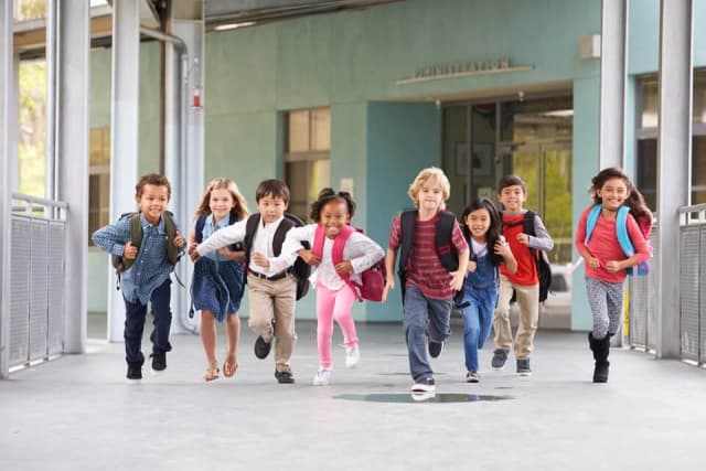 A group of school-age children with backpacks running together down a school walkway