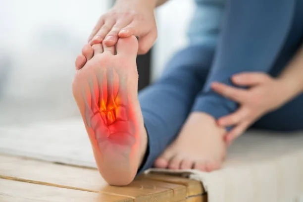 A person holding the sole of their foot, with the painful area highlighted in red